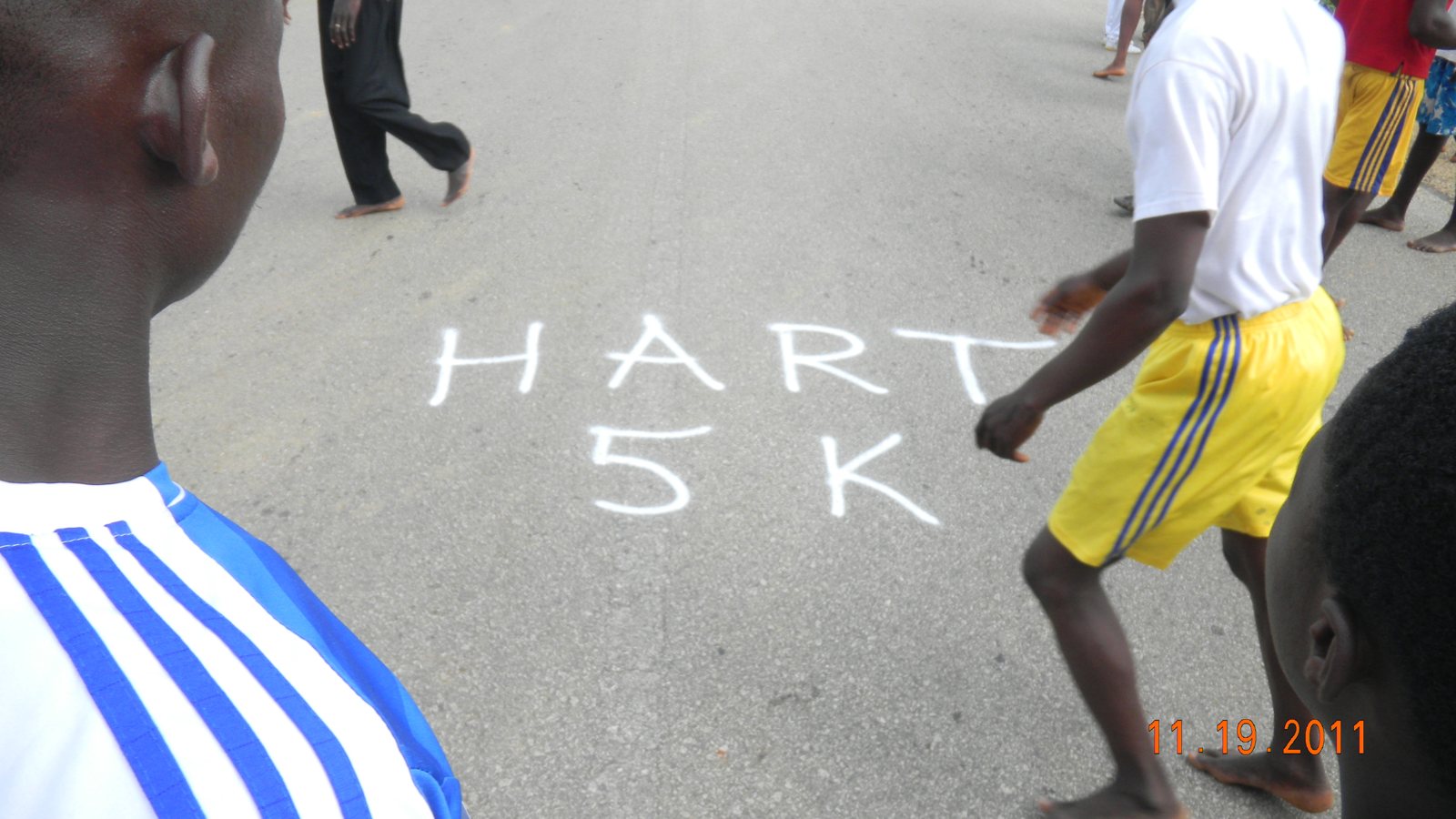 HART 5K painted on the road as barefoot runners cross it at the companion race in Ghana